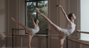 two ballerinas doing ballet moves beside ballet bar