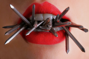 Photograph of a woman's lips chewing on metallic construction nails by Rodolfo Clix